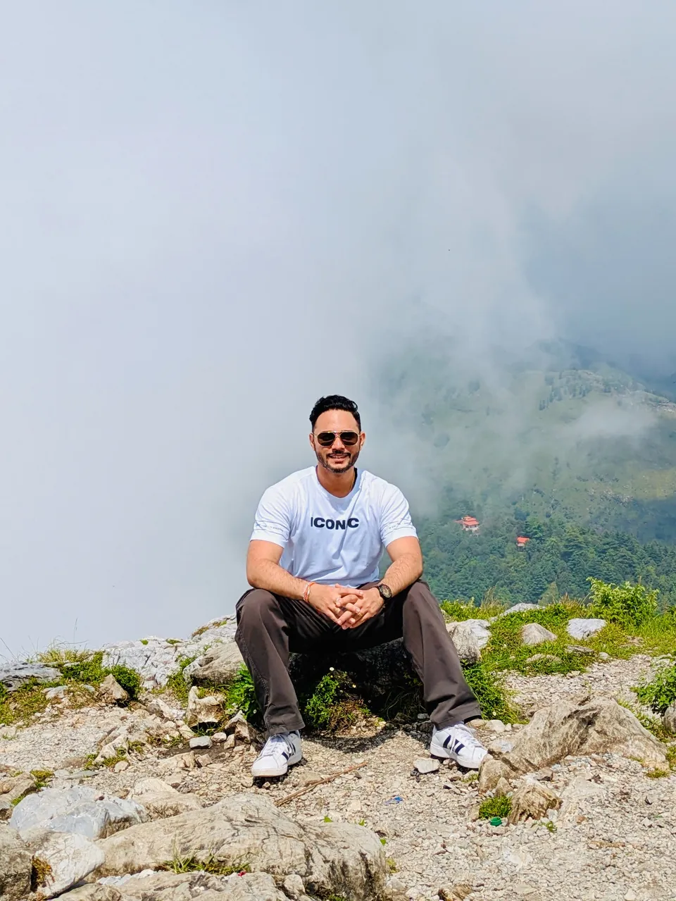 Rahul sitting on a rocky viewpoint with mist rolling over the mountains